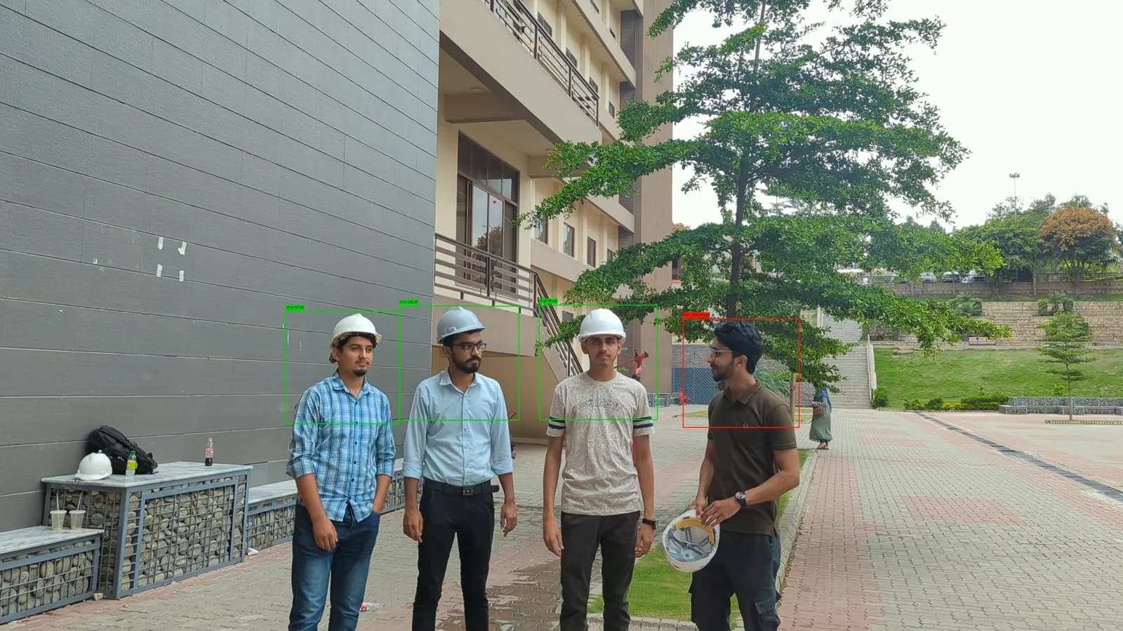 Four workers at close range, three boxed in green and labelled Hardhat and the fourth boxed in red and labelled No-Hardhat while holding his helmet